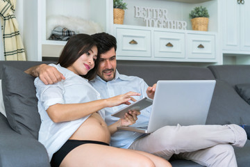 The pregnant woman encourages her husband who is working in the living room at home.