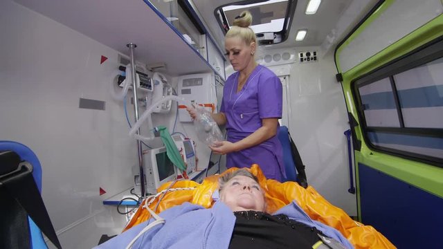 Emergency Medical Services. Paramedic Provides Critical Care To The Patient. Ambulance Car Interior. Nurse Prepares Oxygen Mask For An Elderly Woman.