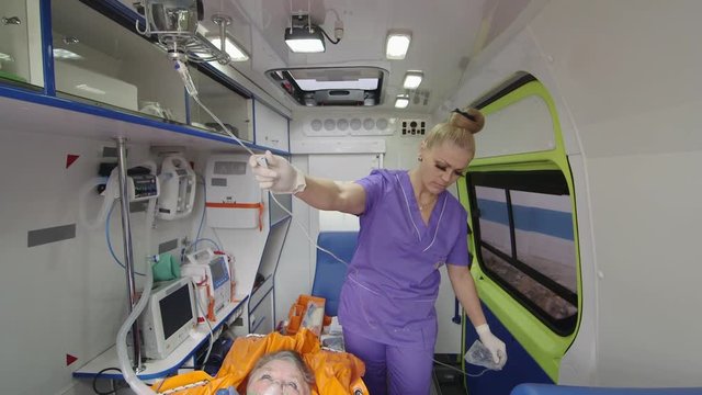 Emergency medical service. Female paramedic treating elderly patient in ambulance during transport. Ambulance vehicle interior.