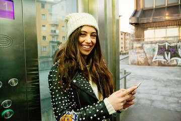 Urban young woman using phone on elevator