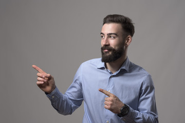 Young modern stylish bearded millennial business man showing fingers presenting blank copyspace against gray background. 