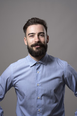 Obraz premium Vertical headshot of proud successful confident bearded businessman with arms on hips smiling at camera against gray studio background.
