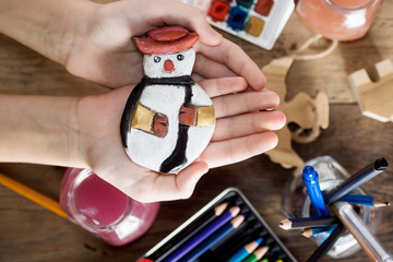 Top view child's hands holding vintage christmas toys. Paints and brushes on table in background. Kids activity concept. New year