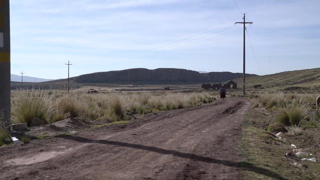 Day woman walks up rural dirt road outskirts of village in Peru, near Juliaca