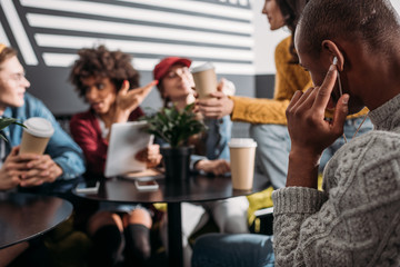 young man listening music with earphones while his friends blurred sitting on background