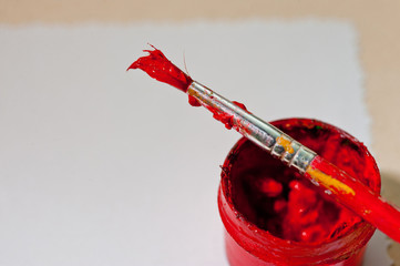 A jar with red paint and a brush on a sheet of white paper