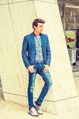 Obraz premium Man Casual Urban Fashion. Wearing blue blazer, patterned under shirt, jeans, fashionable sneakers, a young European guy standing by column, waiting for you to shopping outside store. .