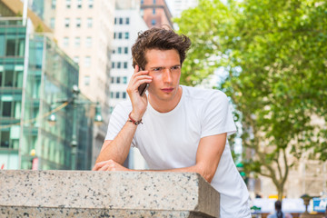 European college student traveling in New York. Wearing white T shirt, a young guy looking down, thinking, calling on his mobile phone outside on street in summer. Technology in our daily life..