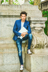 Serious European college student studying in New York. Wearing blue blazer, jeans, sneakers, holding a laptop computer, a young guy standing at the corner on campus, waiting for you. .