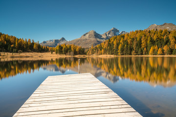 beautiful mountain lake near St. Moritz with reflections of autumn and a wooden pier in the foreground and mountain peaks behind