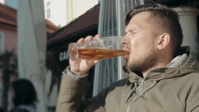 Young Man Drinking Glass of Beer In a Street Restaurant. Man Enjoys Beer In a Cafe On The Street On a Sunny Day
