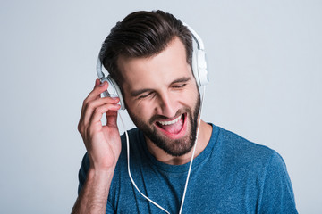 His favorite song. Portrait of handsome young man listening to music in headphones with smile while standing against white background