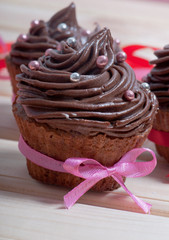 Chocolate cupcake with chocolate cream, decorated with ribbon, on a wooden background. Valentine's Day.