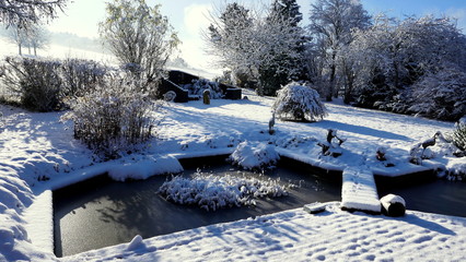 sonnige, winterliche Gartenanlage mit Teich an Terrasse angrenzend 