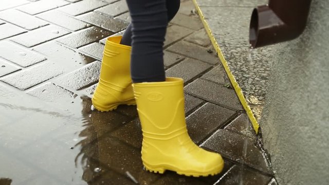 A little girl in yellow rain boots is standing in a puddle.