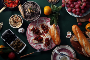 Set of various unusual appetizers: pate, olives, hummus, marinated plums with soft cheese on baguette and chiabatta slices. Old painters lighting style.