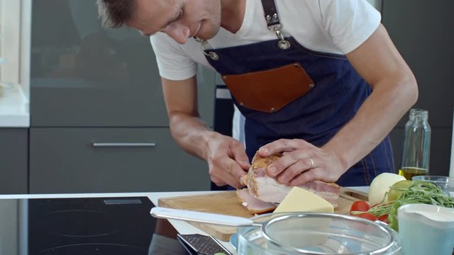 Handheld shot of male professional chef slicing bacon and talking while cooking in kitchen