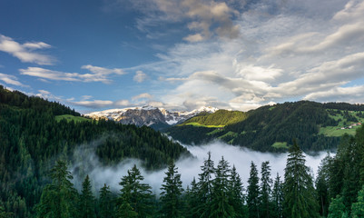 Naklejka na ściany i meble moorig in the Italian Dolomites near Alta Badia with forest and clouds in the valley and beautiful mountains behind