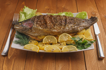 Fried fish on a white plate. Baked potatoes, lemon. Dill. Fork. Ready to use.