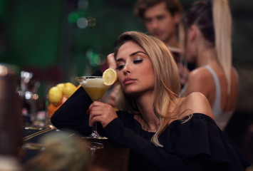 Young woman sitting alone in bar with a coctail