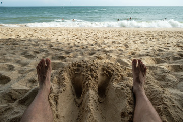 Close up of a man feet relaxing on an tropical beach near the sea. Concept of rest or vacation in summer