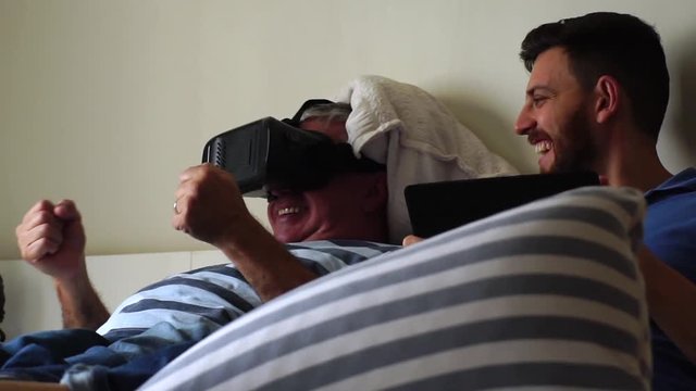 Friends/Father and Son Lying Down and Having Fun with VR Googles and Tablet