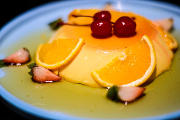 Vanilla pudding with two orange slice, three strawberry slice; and three cherry on top as a decoration