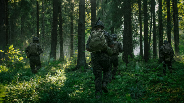 Fully Equipped Soldiers Wearing Camouflage Uniform Attacking Enemy, Rifles Ready to Shoot. Military Operation in Action, Squad Running in Formation Through Dense Smokey Forest. Back View Footage.