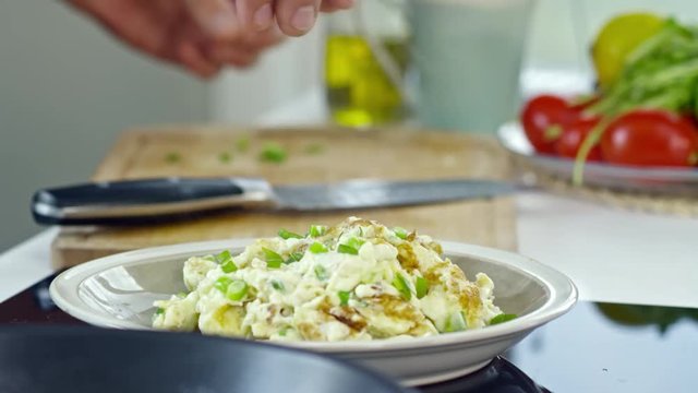 Close up of hands of male cook adding chopped spring onion to tasty scrambled eggs on plate