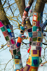 knitted woollen yarn bomb tree with baubles and blue sky background