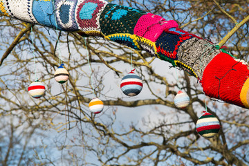 knitted woollen yarn bomb tree with baubles and blue sky background