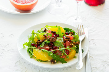 Fresh salad with arugula, orange, grapefruit, walnuts and pomegranate seeds on white table cloth. Healthy food.