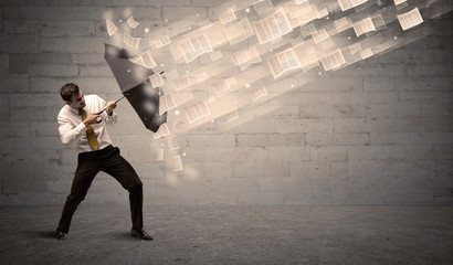 Business man protecting with umbrella against wind of papers