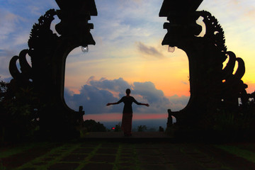Silhouette of woman full length with arms wide open at the balinese traditional gates at the top of Pura Besakih at sunset.