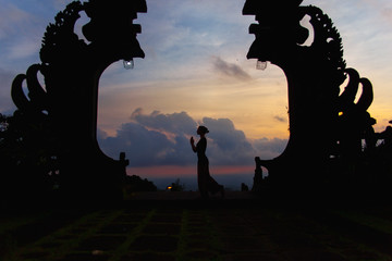 Silhouette of woman full length at the balinese traditional gates at the top of Pura Besakih at sunset.
