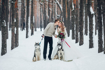 Fototapeta na wymiar Cute couple with two siberian husky are posed on background of snowy forest. Winter wedding. Artwork