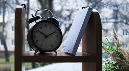 Alarm clock and book on the bookshelf by the window