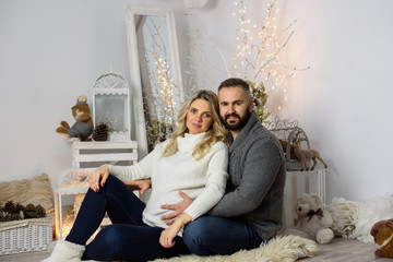 Obraz premium Beautiful pregnant couple in love on a Christmas, having a rest on Christmas holidays before the new year. Big pregnant belly