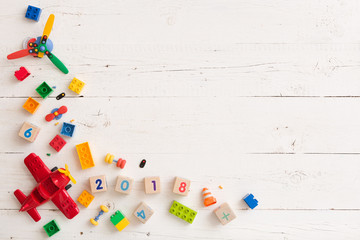 Top view on children toy plane, colorful plastic bricks and wooden cubes on white wooden background.