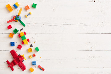 Top view on multi-color toy bricks on white wooden background. Children toys on the table.