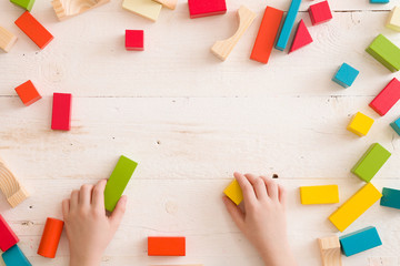 Top view on child's hands playing with colorful wooden bricks on white table background. Boy building with wooden constructor. Education concept