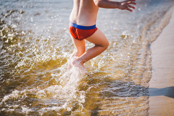 A cheerful male child of three years running along the beach near the water and splashing fly. Active Recreation In summer near the river