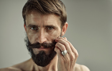 Portrait of middle-aged handsome man with bare shoulders. Lush and dense beard and moustache in a...