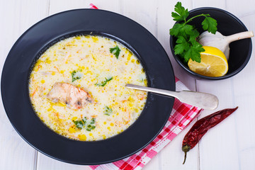 Creamy soup with salmon in black plate on white wooden table