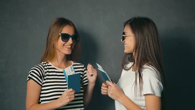 Thrilled girls with tickets and passports smiling and showing tumbs up in the grey background with travel animation icons