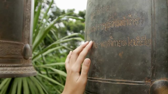 Woman touches textured lettering on sacral bells in Wat Saket Ratcha Wora Maha Wihan, the Golden Mount . Bangkok Thailand.