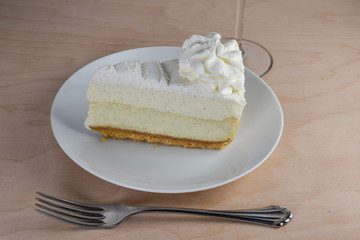 Isolated vanilla bean cheescake with a layer of whipped cream and fork on a hickory wood table