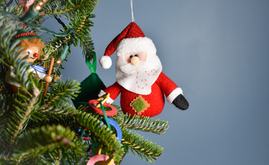 Stuffed Santa Claus  ornament hanging at edge of a decorated Christmas tree with room for text or copyspace.