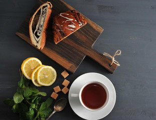 roll with poppy seeds, tea, lemon and mint on wooden background