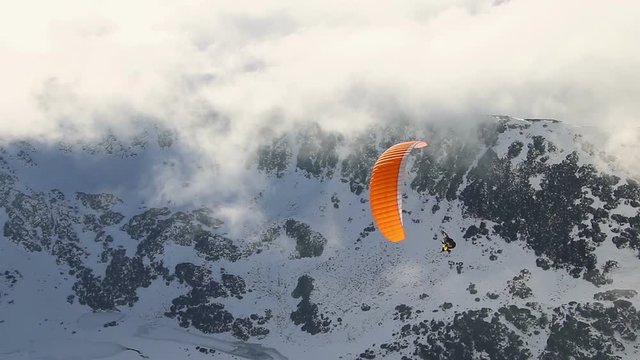 Paragliding above mountain peaks and clouds during winter sunny snowy day